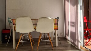 Ein Zimmer mit zwei weißen Stühlen, Holzboden, einer Deckenleuchte und einer Glastür zum Balkon.