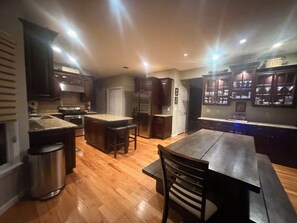 A kitchen with wooden cabinets, a stainless steel refrigerator, a wooden dining table, and a bar area with a countertop.