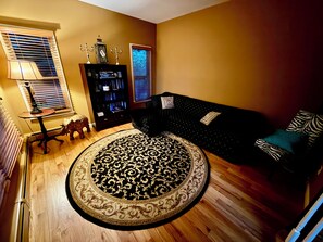 A living room with a round patterned rug, a dark sofa with patterned cushions, a bookshelf, and a lamp.