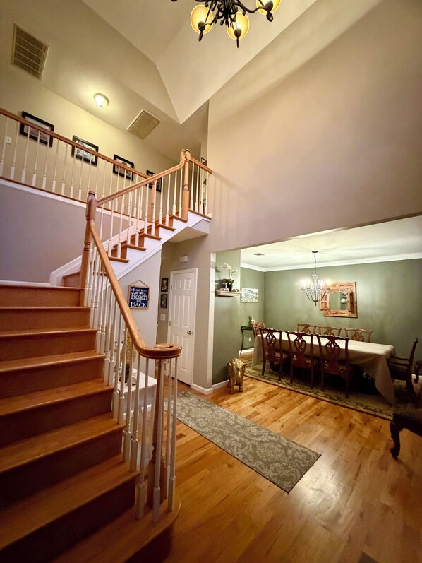 A spacious living area with a wooden staircase, a dining table, and a chandelier.