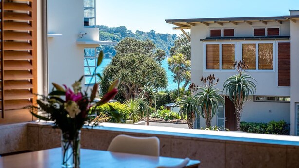 A dining area with a view of a coastal landscape, including trees and a building with large windows.