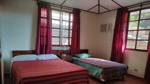 A bedroom with two beds, a nightstand, a lamp, and a window with curtains.