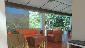 A spacious patio with wicker furniture, a white bench, and a view of lush greenery.