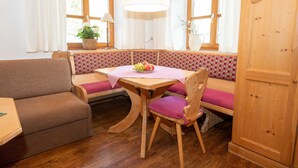 A cozy room with a wooden table, a bench with a checkered cushion, a wooden cabinet, and a window with curtains. - 1 Appartement , Balkon, Kochnische, 1 Wohn-/schlafzimmer, max 2 Pers, Wlan (Ruhpolding)