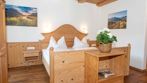 Un lit en bois avec une tête de lit, une table de chevet ornée d’une plante et deux lampes fixées au mur.