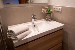 Ein modernes Badezimmer mit Waschbecken, einem Spiegel darüber und einer Holzkonsolen-Schublade.