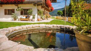 A traditional chalet with a stone fountain, a well-maintained lawn, and a balcony adorned with red flowers. - 4 Fewo , Balkon, Kochnische, 1 Schlaf- und 1 Wohn-/schlafz. max 4 Pers, Wlan (Ruhpolding)