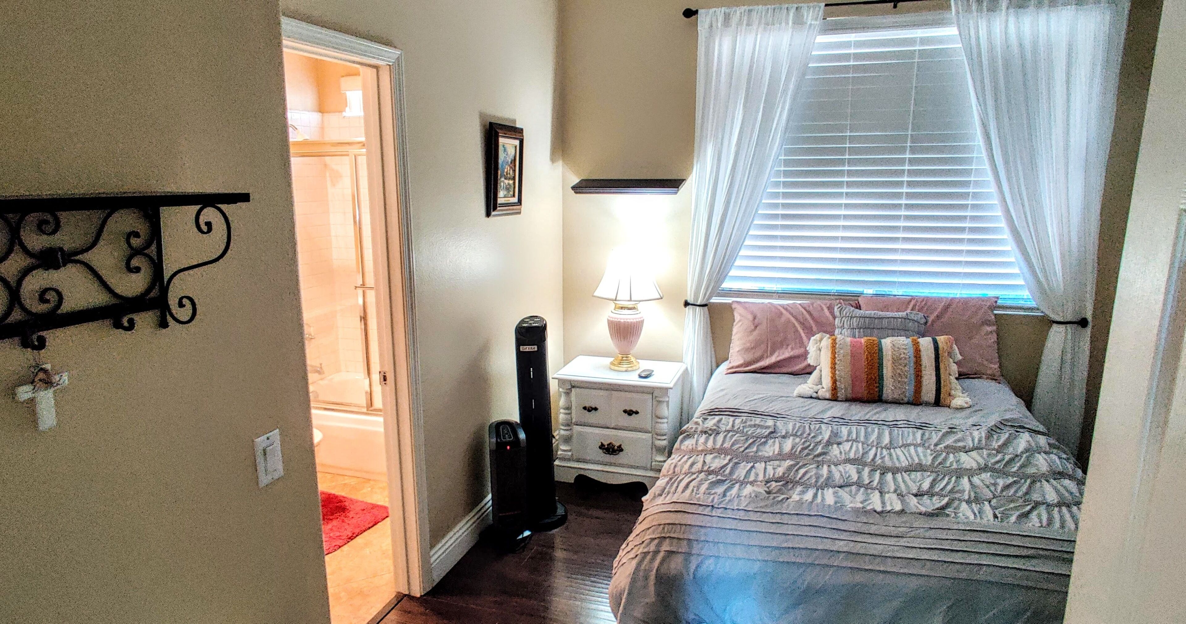 Une chambre à coucher comprenant un lit, une table de chevet, une lampe, une commode et une porte donnant sur une autre pièce.