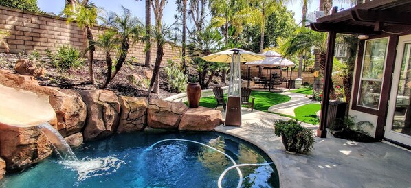 A backyard with a swimming pool, a waterfall feature, and outdoor furniture.