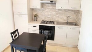 A compact kitchen with a gas stove, oven, and sink. There is a dining table with chairs. - Cristina Garden (Pisa)