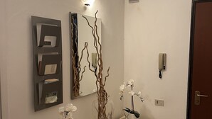 A modern hallway with a light fixture, a mirror, and a vase with branches and orchids. - Cristina Garden (Pisa)