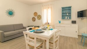 Ein Wohnzimmer mit einer Couch, einem Esstisch, Stühlen, einem Fernseher und einem Schrank.