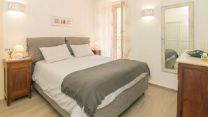 Ein Schlafzimmer mit einem Bett, Nachttischen, einem Spiegel und einer Tür zu einem anderen Raum.