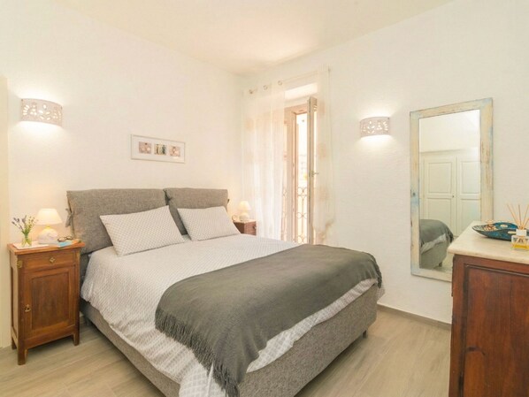 A bedroom with a bed, bedside tables, a mirror, and a door leading to another room.