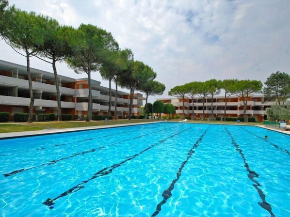 A swimming pool with clear blue water, surrounded by multi-story buildings with balconies and trees.
