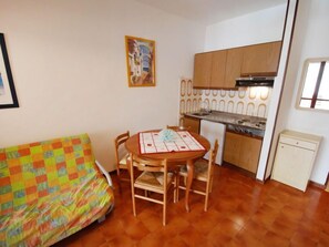Un espacio habitable compacto con kitchenette, una mesa de comedor con sillas, un sofá colorido y un cuadro en la pared.