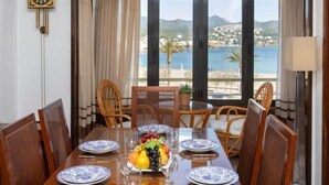 A dining area with a table set for four, a clock on the wall, and a view of the sea and mountains.
