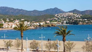 A coastal town with buildings on a hillside, a beach, and palm trees.
