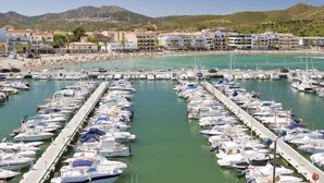 A marina with numerous boats docked in rows, a beach with people, and buildings in the background.