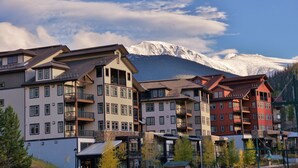 Een meerlaags hotel met balkons, een skipiste op de achtergrond en een bergketen.