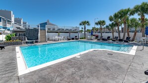 Une piscine entourée de bâtiments dotés de balcons, avec des chaises longues et des palmiers.