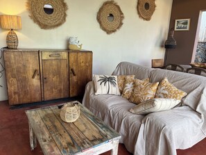 A cozy living room with a wooden cabinet, a woven coffee table, and a sofa with tropical-themed cushions.