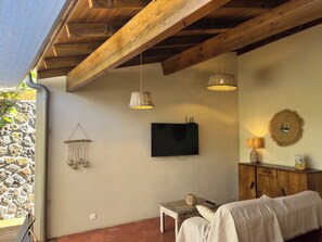 A cozy room with a stone wall, wooden ceiling beams, a flat-screen TV, a woven lamp, and a rustic cabinet.