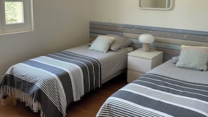 A bedroom with two single beds, a bedside table with a lamp, a window with blinds, and a mirror on the wall. - MATOUNE pleasant, 4/6 person house near Lake Leon  (Léon)