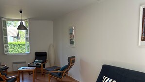A modern living room with a dark blue sofa, wooden coffee table, and two rocking chairs. A large window provides a view of greenery outside. - MATOUNE pleasant, 4/6 person house near Lake Leon  (Léon)
