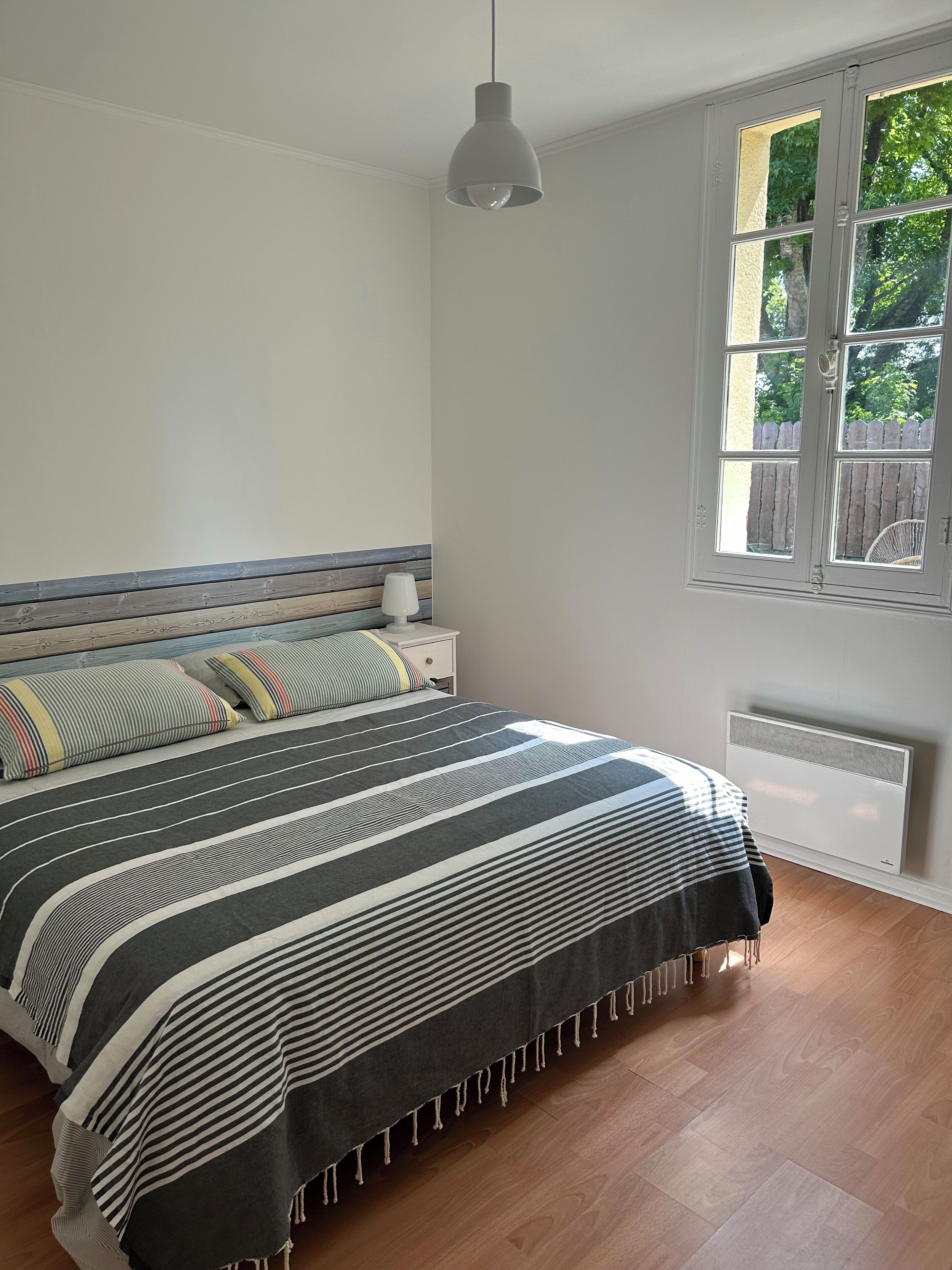 Une chambre à coucher avec un lit, une table de chevet, une lampe, une fenêtre et un radiateur.