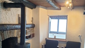 A cozy room with a wood-burning stove, two chairs, a window, and a stone wall. - Mountain worlds behind Lake Maggiore (Falmenta)