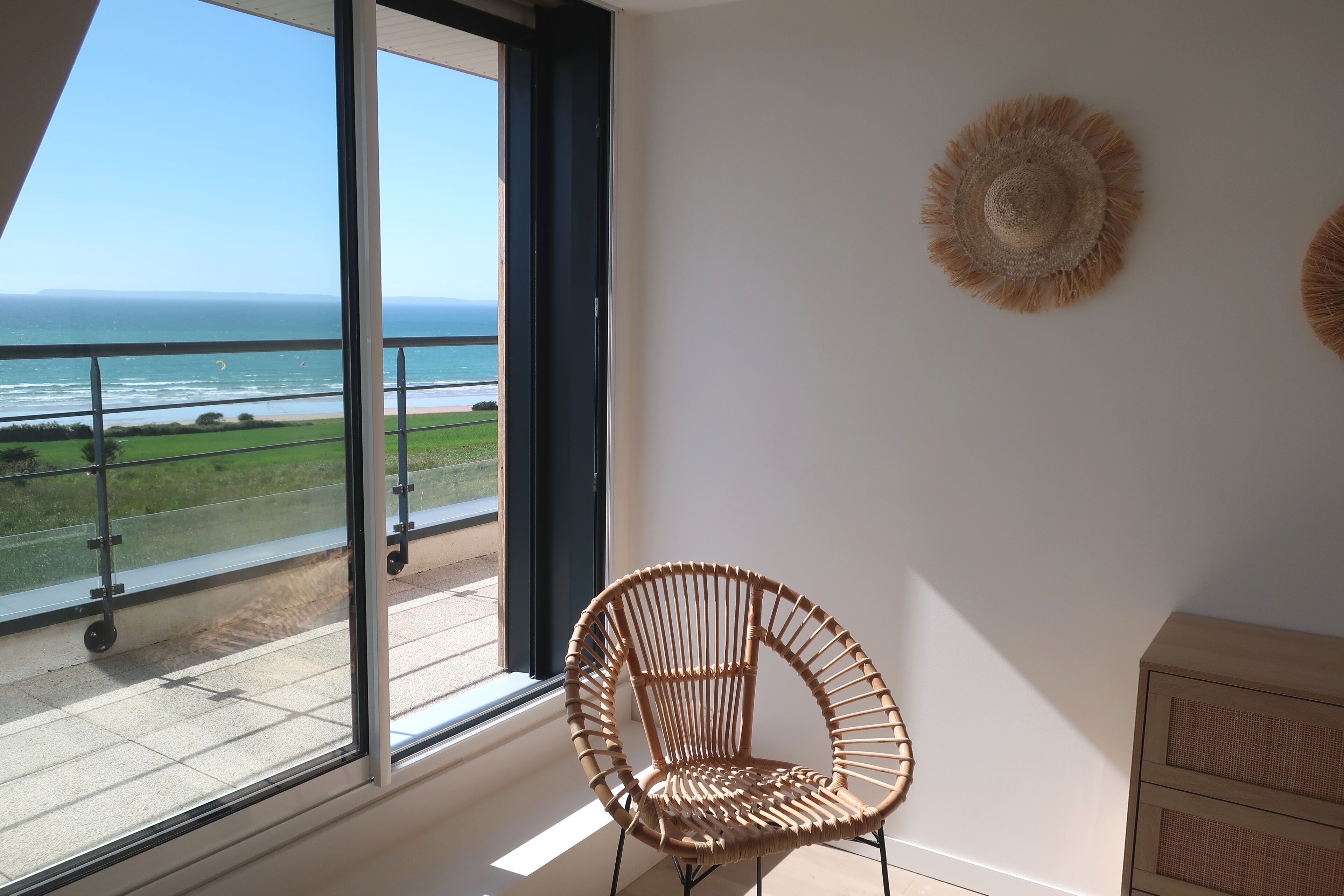 Un balcón con vista al océano, una silla de mimbre y un mueble de madera.