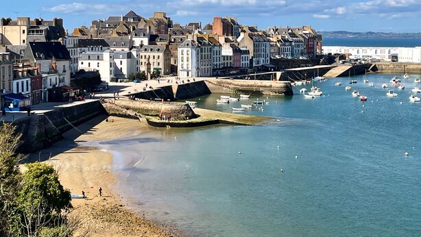A coastal town with historic buildings, a sandy beach, and a harbor with boats.