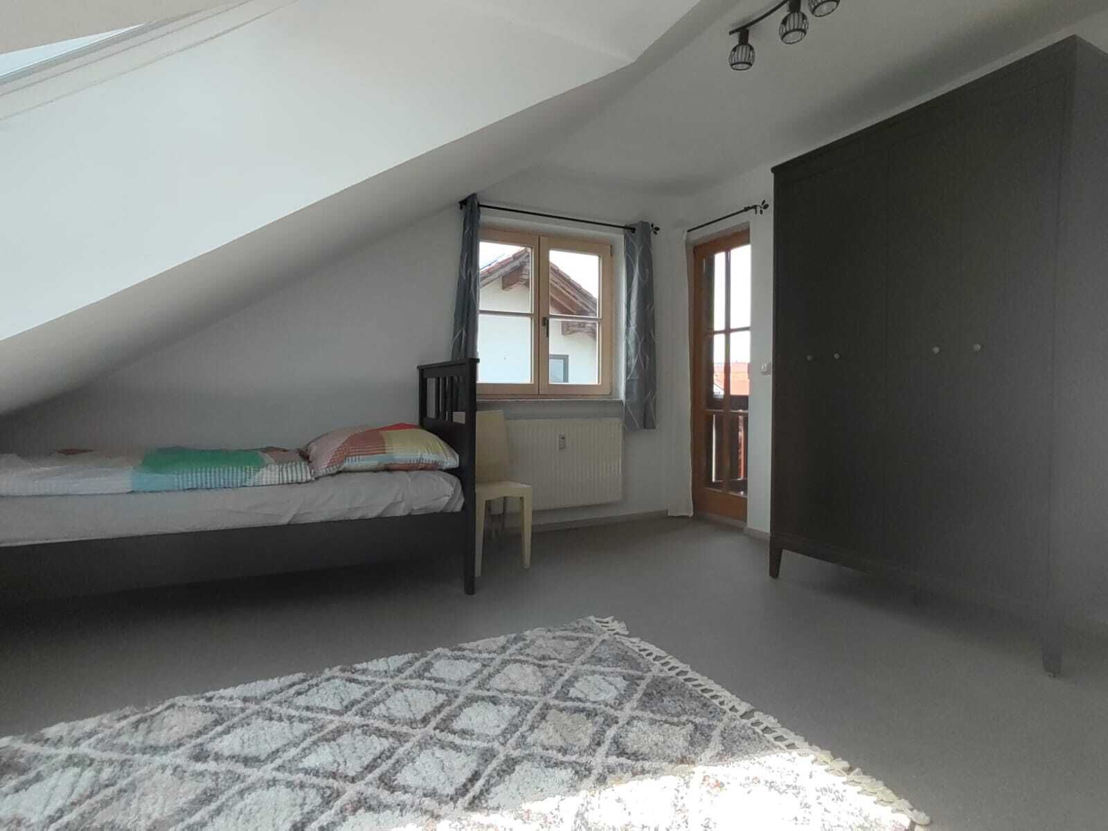Een kleine kamer met een schuine kap, een bed, een stoel en een kledingkast.