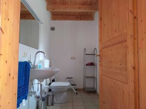 Ein kleines Badezimmer mit einem weißen Waschbecken, einer Toilette und einem Metallregal.
