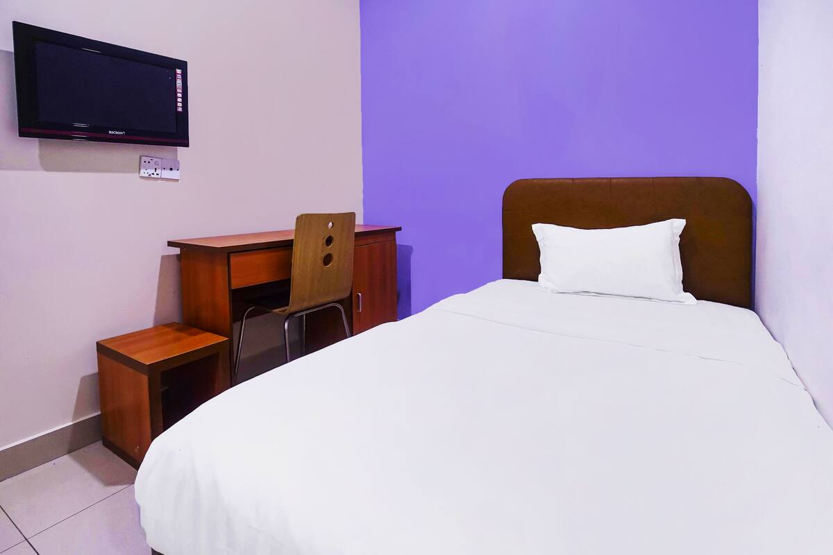 A hotel room with a bed, a desk with a chair, a television mounted on the wall, and a power outlet.