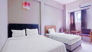 A hotel room with two beds, a chair, a table, and an air conditioning unit.