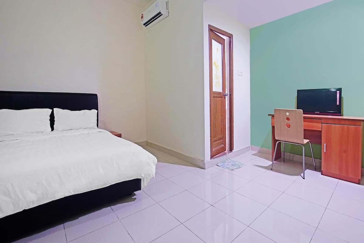 A bedroom with a bed, a desk with a chair, a television, and an air conditioning unit.