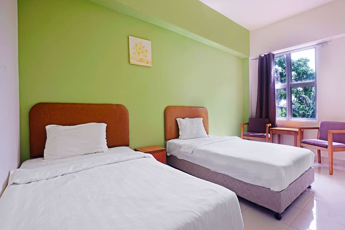 A hotel room with two beds, a window with curtains, a chair, and a small table.
