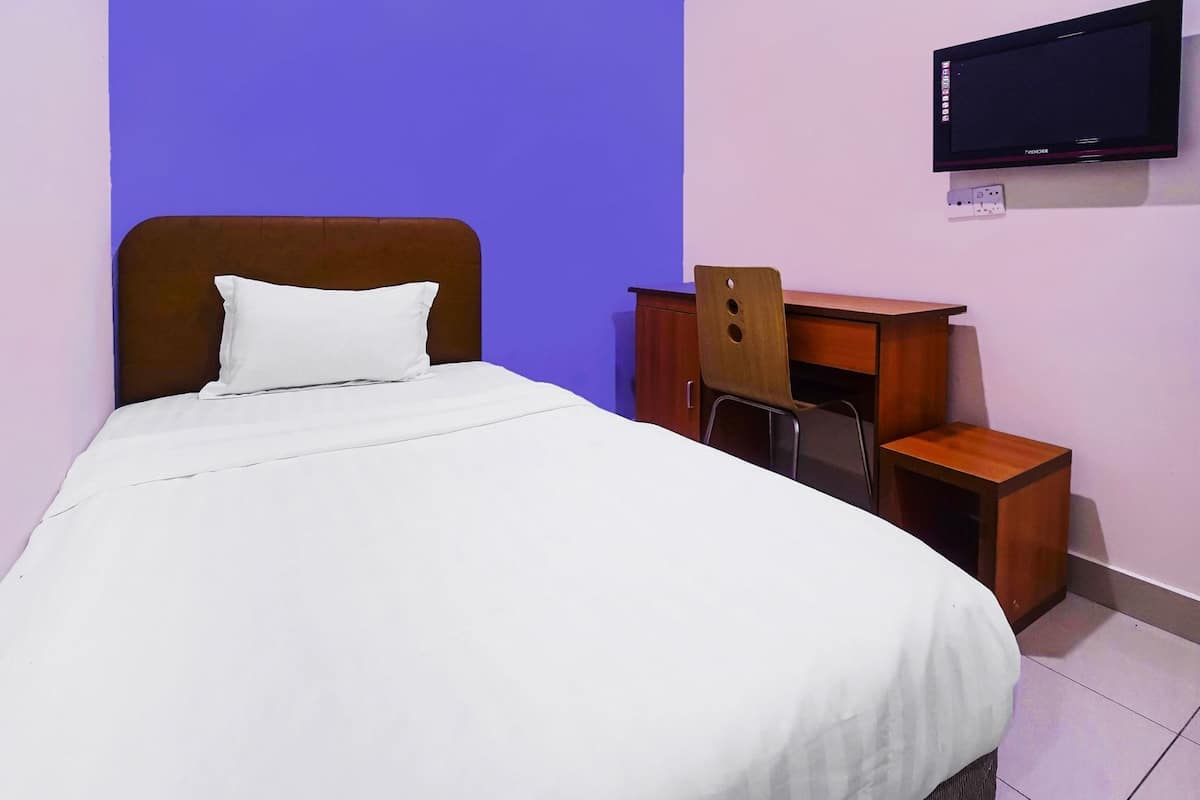 A neatly made bed with a white sheet and pillow, a wooden nightstand with a chair, and a flat-screen TV mounted on the wall.