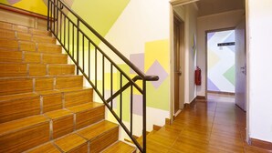 A staircase with wooden steps and black railings, leading to a hallway with a geometric wall design and a fire extinguisher mounted on the wall.