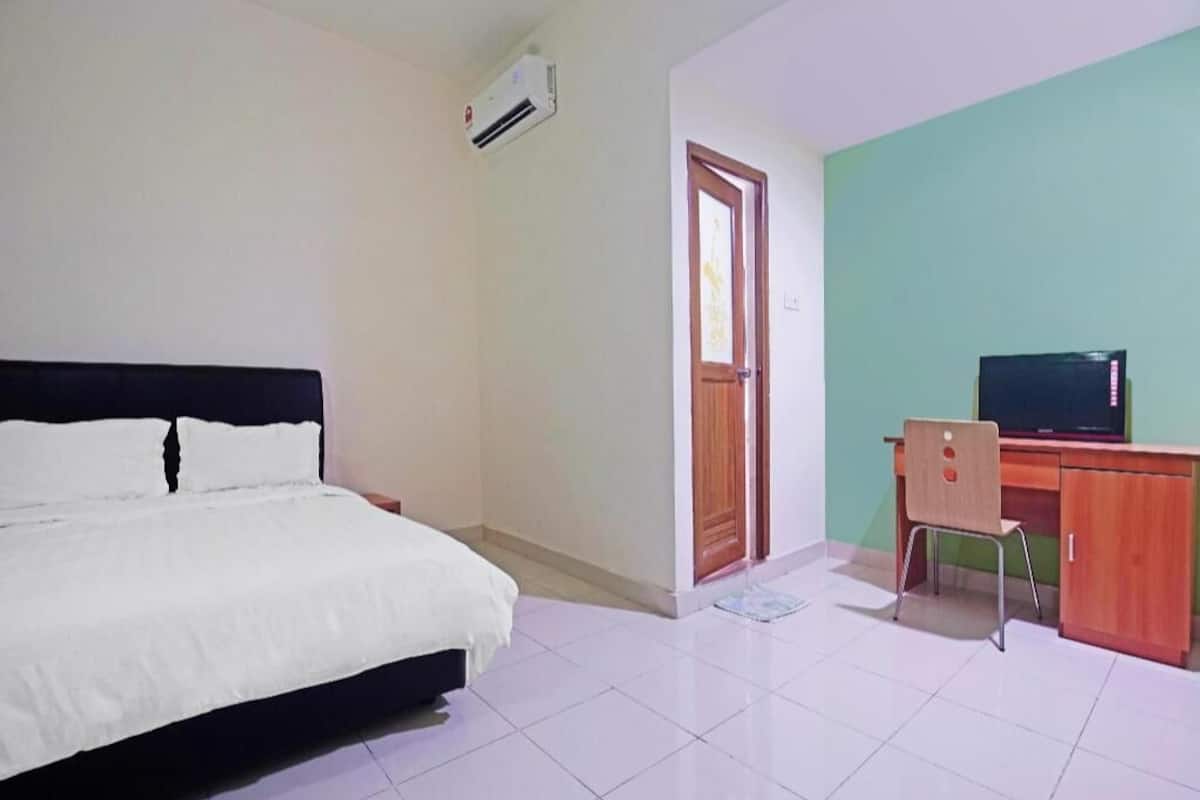 A bedroom with a bed, a desk with a computer, a door, and an air conditioning unit.