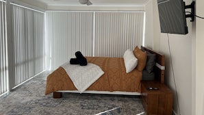 A bedroom with a bed, a ceiling fan, a TV, and a window with blinds. - 'The Savoy'. Central home with pool. Pet friendly (Port Macquarie)