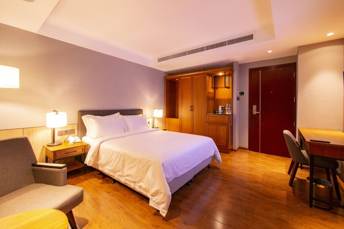 A hotel room with a bed, bedside tables, a desk, a chair, and a wardrobe.