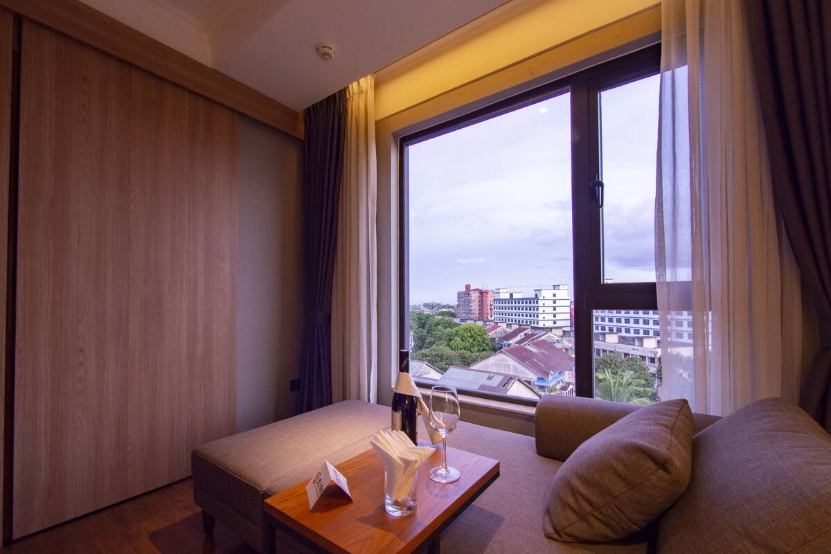 A hotel room with a large window, a sofa, a small table with a wine glass, and a wooden floor.