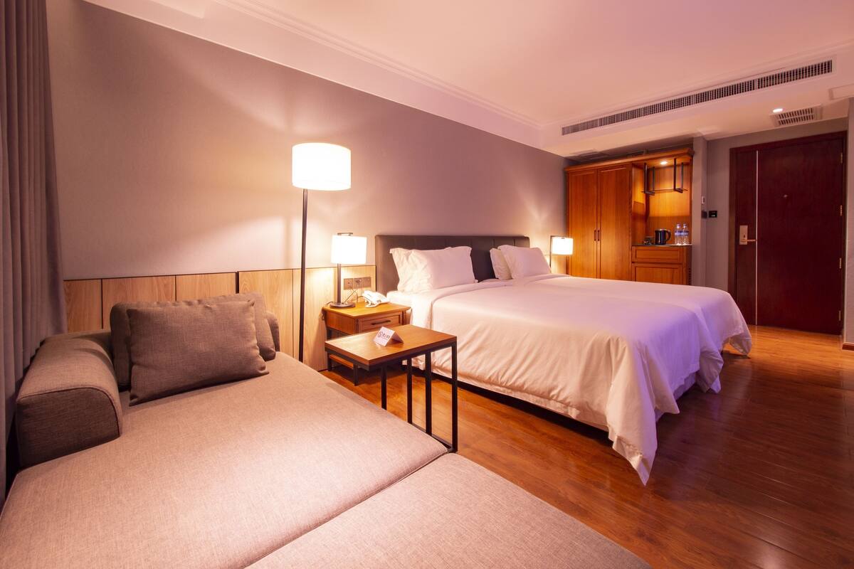 A hotel room with a bed, a sofa, a nightstand, a lamp, and a wardrobe.