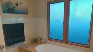 Ein Badezimmer mit einer Badewanne, einem Handtuchhalter, einem Topfpflanzen und einem Fenster mit satiniertem Glas.