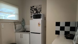 Eine kleine Küche mit Kühlschrank, Mikrowelle, Spüle und Mülleimer.