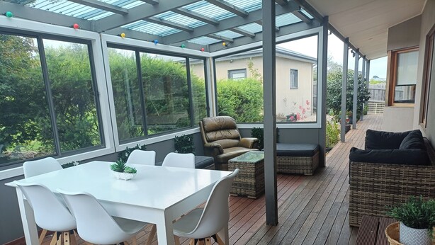 Eine überdachte Terrasse mit Tisch und Stühlen, einer Couch und einer Korbsitzbank.