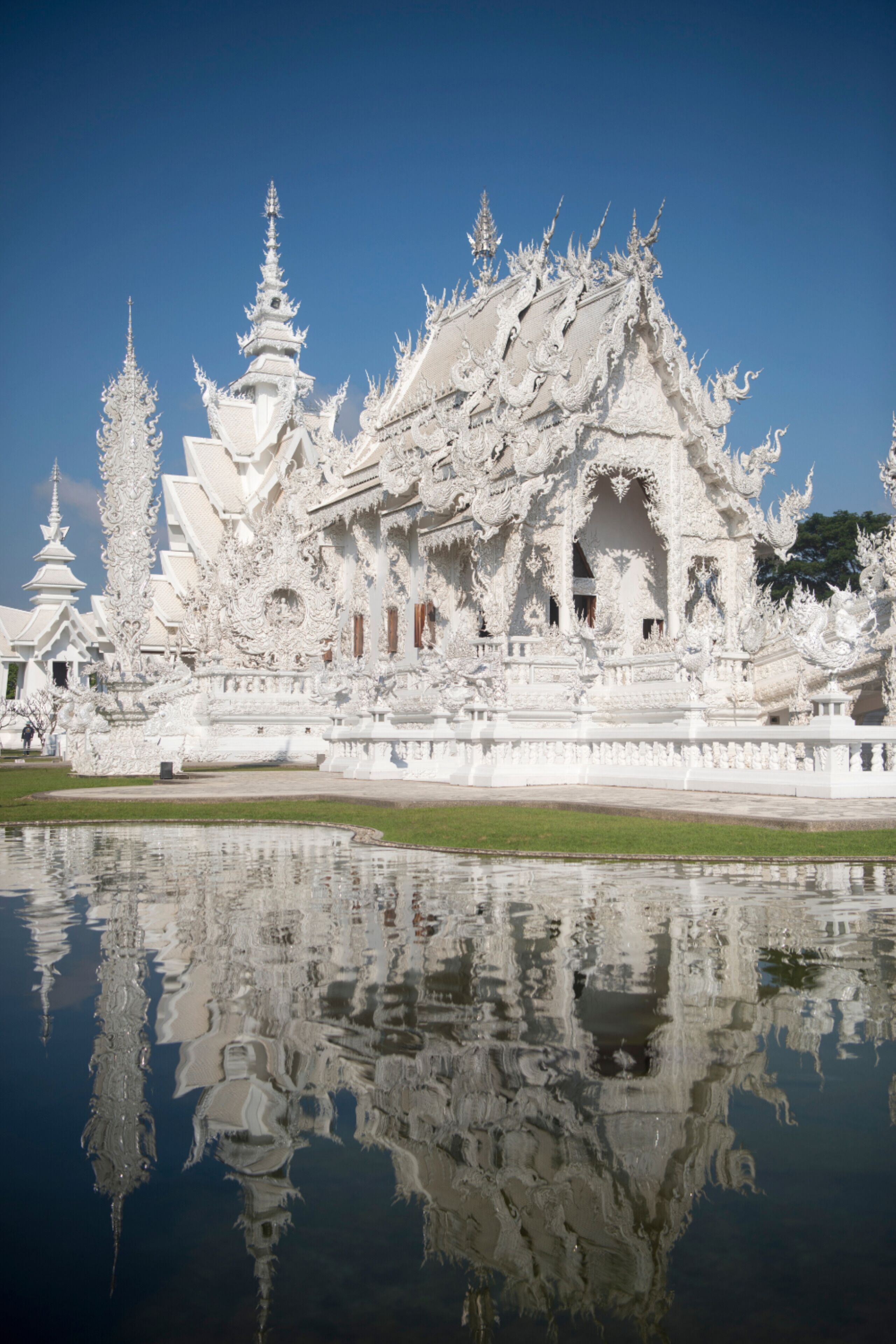 A white ornate temple with multiple tiers and spires, surrounded by a calm reflective pond.